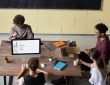 Four diverse colleagues engaged in a team meeting, working on laptops with coffee and notes, fostering collaboration. — How T
