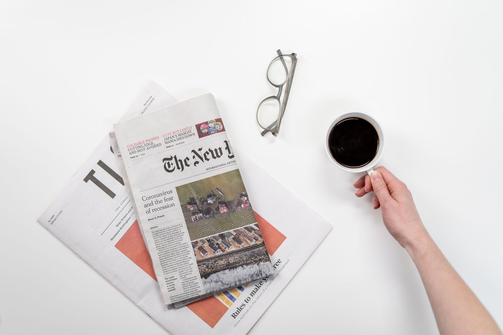 Top view of a coffee cup, newspapers, and eyeglasses on a clean white desk — Vavada promokoodid ja kasutamise juhised 2026